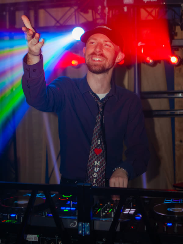 DJ behind the decks with a hand raised at Dress to Impress, photographed by Jay Snaps