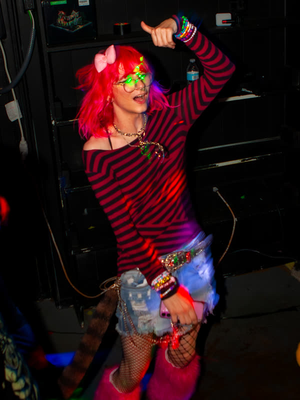 Guest posing in a striped top and red wig at Dress to Impress, photographed by Jay Snaps